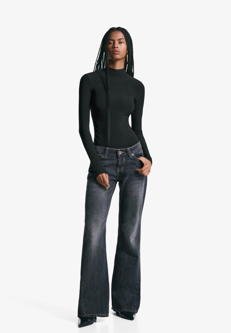 Svart långärmad bodysuit med hög halsringning, parat med mörka utsvängda jeans. Förslitna denim med standard femficksdesign och framknapp.