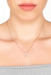 Rose gold necklace featuring a floral pendant with a textured outline and small clear gemstones, worn on bare skin.