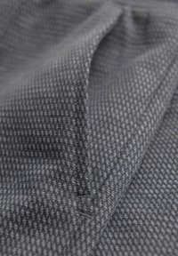 Nahaufnahme eines grauen, strukturierten gewebten Stoffes mit einer kleinen Naht und leichter Falte, die das Strickmuster zeigt.