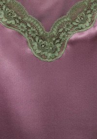 Tessuto di satin viola con un bordo in pizzo verde. Il pizzo presenta motivi floreali e bordi a scallop, evidenziando texture e dettagli di design.