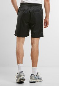 Shorts de sport noirs avec une taille élastique, dotés d'une poche arrière et de rayures latérales contrastées. Fabriqués dans un matériau lisse et léger.