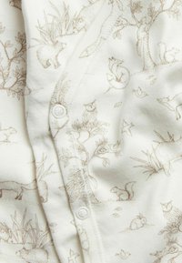 Weißer Baumwollstoff mit braunen Illustrationen von Tieren und der Natur; verfügt über Knöpfe und eine glatte Textur mit detailreichen Mustern von Bäumen und Wildtieren.