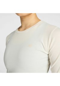 Lichtbeige langemouwtop gemaakt van ribgebreide stof, met een ronde halslijn en een klein, subtiel logo op de linkerborst.