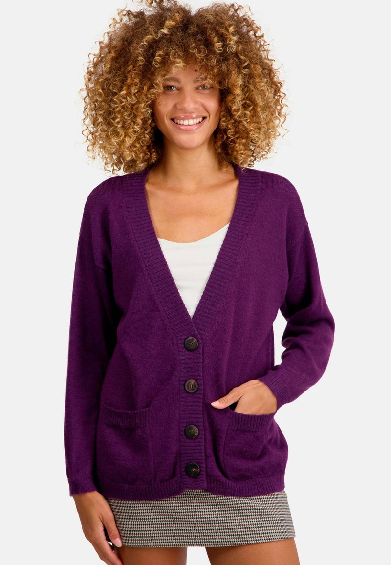 Cardigan violet en tissu tricoté doux, avec un col en V, une fermeture à boutons, deux poches avant et des poignets côtelés.