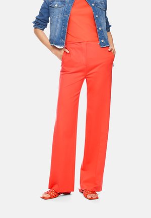Woman wearing bright orange wide-leg pants and matching open-toe sandals, paired with a cropped blue denim jacket, hands in pockets.
