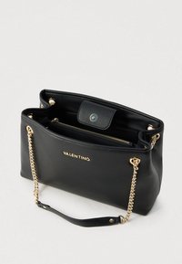 Crna kožna torba sa zlatnom metalikom, naramenicom s lancem i utisnutim logotipom. Ima presvučeni unutrašnjost s džepom na patentni zatvarač za organizaciju.