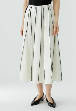 Witte midirok met verticale zwarte strepen, gedragen met zwarte puntige slingback-schoenen en een zwarte top.