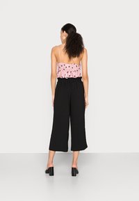 Calças largas pretas com uma cintura elástica, combinadas com um top de alças smock rosa com padrões florais. Design simples e descontraído.