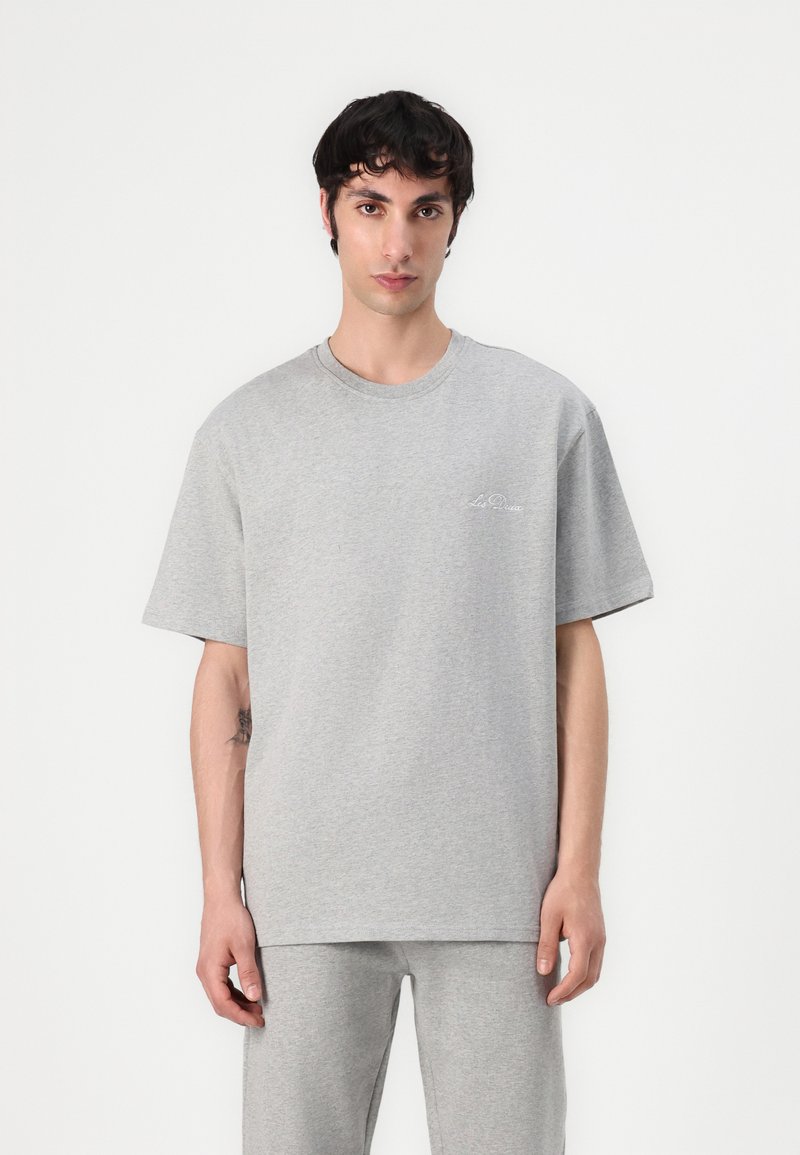 Tricou din bumbac gri, cu mâneci scurte, decolteu rotund și broderie logo subtilă pe pieptul stâng, asortat cu pantaloni gri.