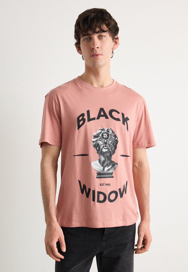 Růžové bavlněné tričko s grafikou poprsí a textem "BLACK WIDOW" uvedeným tučnými černými písmeny a datem 1993.