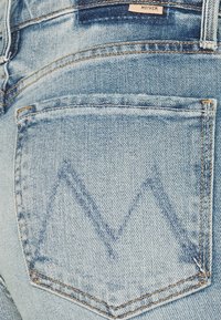 Ljusblå denimjeans med en ensam bakficka som har ett sydd V-format mönster. Tyget har ett blekt utseende med synlig sömnad.