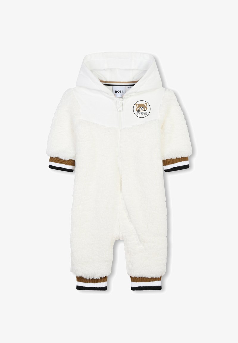 Combinaison en peluche blanche avec capuche, dotée de poignets rayés marron et noir, et d'un patch rond avec un logo sur la poitrine. Fermeture éclair.