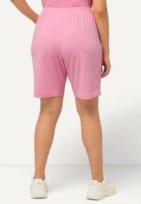 Pantaloni corti di cotone rosa con vita elasticizzata, che arrivano a metà coscia. Texture morbida e design semplice, abbinati a sneakers bianche.