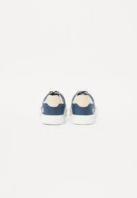 Blue sneakers with a textured fabric upper, cream accents on the heel and tongue, white rubber sole, and traditional laces.