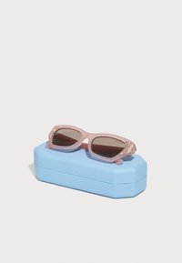 Ochelari de soare roz cu lentile închise au un accent sclipitor pe brate, expuși deasupra unei cutii rectangulare de culoare albastru deschis.