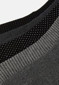 Sammlung von gestrickten Kleidungsstücken in verschiedenen Schwarztönen und Grautönen, mit gerippten, gepunkteten und Fischgrätmustern auf den Stoffen.