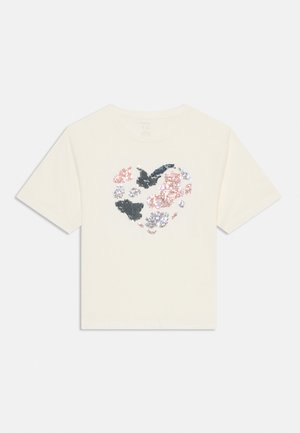 T-shirt crème à manches courtes avec un design de cœur en sequins multicolores de rose, gris et bleu. Col rond classique.