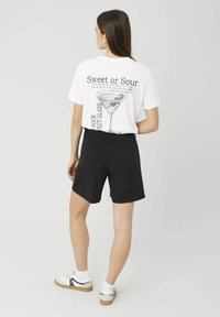 T-shirt blanc avec un imprimé graphique représentant un cocktail et du texte, assorti à un short noir et des baskets blanches avec des accents noirs.