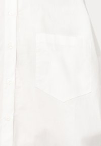 Détail d'une chemise blanche boutonnée montrant un gros plan sur la poche poitrine et les boutons sur la patte de boutonnage avant.