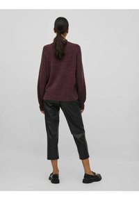 Vínový pletený svetr volného střihu s žebrovanými manžetami a lemem; doplněný o černé zkrácené kalhoty z umělé kůže a masivní černé boty.