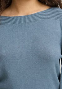 Jasnoniebieski sweter na drutach z szerokim dekoltem, prążkowaną fakturą na ramionach i gładkim wykończeniem na tułowie.