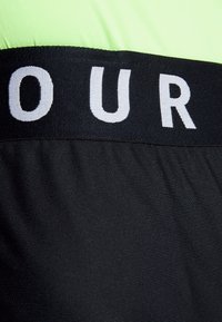 Svart och neon grönt träningsplagg med bred svart midjeresår med vit text, slät textur och kroppsformad design.