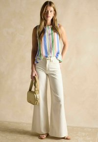 Röstripeeritud ilma varrukateta topp sinises, roosas ja rohelises; koos kõrge vöökohaga valgete avarate pükstega. Mudel hoiab käes väikest kuldset käekotti.