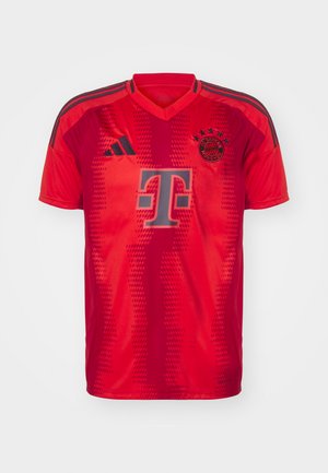 Maillot de football rouge avec un col en V, des manches courtes et un motif texturé. Il comprend un logo gris et trois bandes noires sur les épaules.