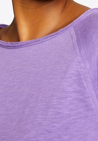 Lavendelfarbenes Kurzarmoberteil mit rundem Halsausschnitt, weichem Textil und sichtbaren Nähten entlang der Kanten.