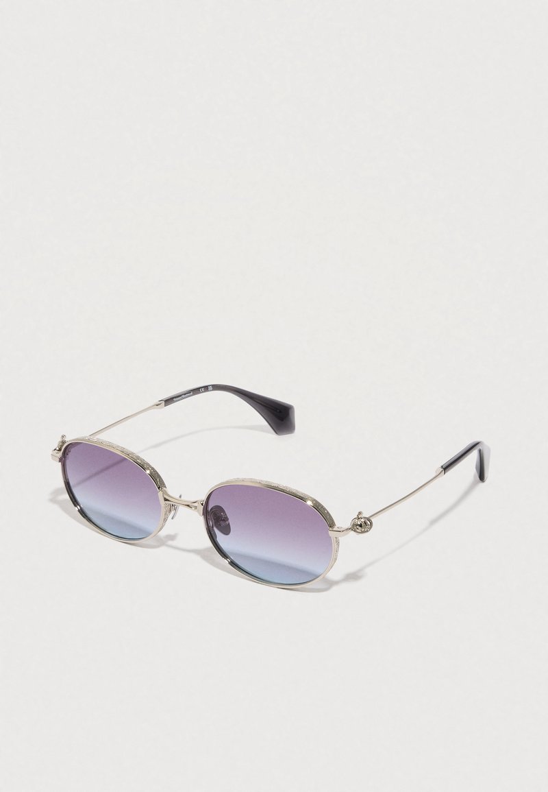 Gafas de sol con un marco ovalado, acentos metálicos plateados, lentes púrpuras degradados y patillas de plástico negro. Presentan detalles texturizados en el marco.