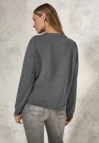 Sudadera gris con escote redondo y mangas largas, hecha de tejido texturizado. Combinada con jeans de mezclilla gris claro.