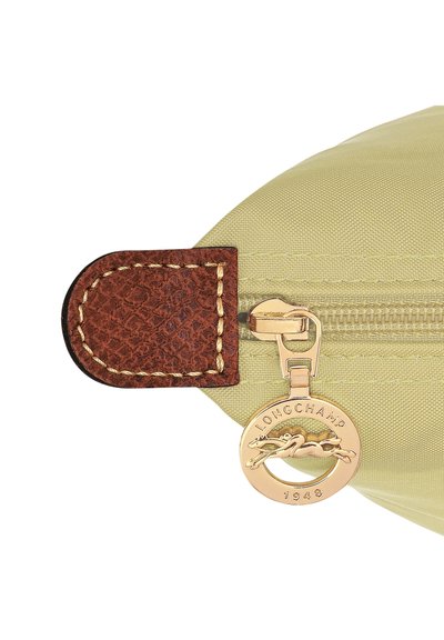 Reißverschlusstasche aus hellgrünem Nylon mit braunem Lederakzent, ausgestattet mit einem goldenen Metallreißverschluss und einem Logotag mit kreisförmigem Design.
