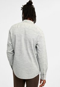 Graues Langarmshirt aus strukturiertem, gemustertem Stoff; Button-Down-Kragen; abgerundeter Saum; detaillierte Nähte; und mit Knöpfen versehene Manschetten.