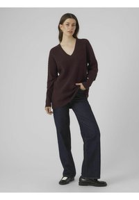 Burgundska v-neck pulover z rebrasto teksturo in dolgimi rokavi, v kombinaciji s temnimi širokimi kavbojkami in črnimi loaferji.
