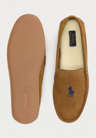 Mocassino slip-on in camoscio marrone con una soffice fodera in fleece, suola in gomma e logo ricamato blu sul lato.