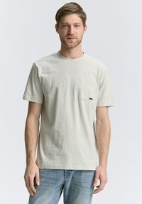 Tricou scurt cu mâneci, de culoare gri deschis, cu un model subtil în dungi, având o buzunar pe piept și un mic logo al mărcii. Poartă-l cu blugi albaștri.