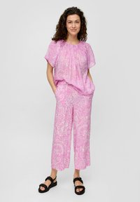 Roze top met bloemenpatroon en een ruime pasvorm, gecombineerd met een broek met wijde pijpen, gemaakt van lichte stof. Zwarte schoenen met een gestructureerde band.