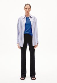 Lichtblauwe gestreepte oversized shirt, blauwe ribbeltop, zwarte uitlopende broek en zwarte slipper sandalen. Stof lijkt glad en casual.