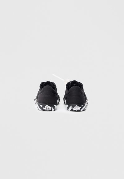Sneakers neri in tela con profilo basso, caratterizzati da una parte superiore testurizzata, lacci bianchi e una suola a strisce bianco e nera con logo sul tallone.