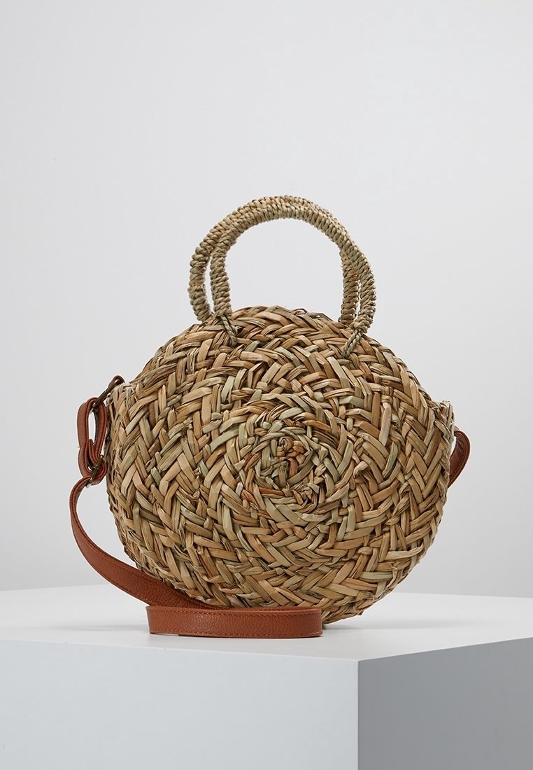 Borsa rotonda in paglia intrecciata con design a spirale, tonalità naturali beige e verde, dotata di due manici e di una tracolla in pelle.
