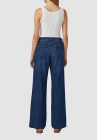Wijduitlopende jeans in donkerblauwe denim, met een hoge taille, twee achterzakken en een nette zoom. Gekleed met een wit tanktop.