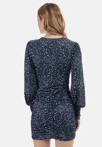 Ruched-mekko tummansinisestä kankaasta, jossa on leopardikuosiset yksityiskohdat. Tämä mekko sisältää pitkät hihat ja tiukan siluetin, joka korostaa vartalon muotoja.