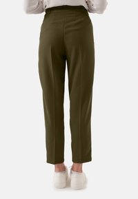 Olijfgroene tapered broek van textuurstof, met een hoge tailleband en achterzakken, gecombineerd met witte sneakers.