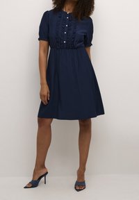 Abito blu navy in tessuto leggero, con maniche corte a soffietto, chiusura frontale con bottoni e volant, e una silhouette a gonna ampia.