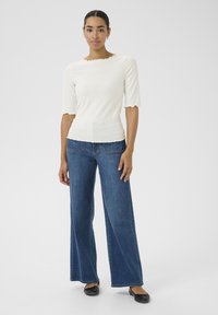 Hvid ribbet top med bølget halsudskæring og ærmer, parret med blå vidde denimjeans med baglommer og syningsdetaljer.