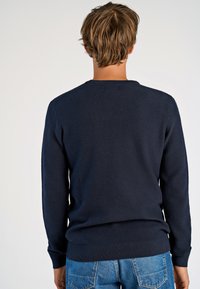Navy Pullover aus Strick mit einem strukturierten Muster, Rundhalsausschnitt und gerippten Bündchen, kombiniert mit hellblauen Jeans.