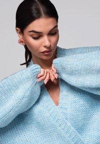 Ljusblå stickad kofta med V-ringning, vida ärmar och textilstruktur. Har mjukt, tjockt garn och en avslappnad passform.