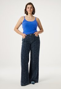 Blauw, zacht tanktop met dunne bandjes, gecombineerd met wijde, gestructureerde, donkerblauwe broek met een gespetterd patroon. De broek heeft zijzakken.