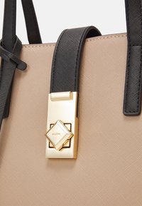 Borsa sintetica beige con manici neri texturizzati e una chiusura decorativa dorata a forma di diamante.