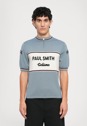 Strick-Polo mit kurzen Ärmeln in Hellblau, ausgestattet mit einem Reißverschluss am Hals, dem auffälligen "PAUL SMITH"-Logo und einem kontrastierenden Band mit "Ciclismo" in Schwarz auf der Brust.